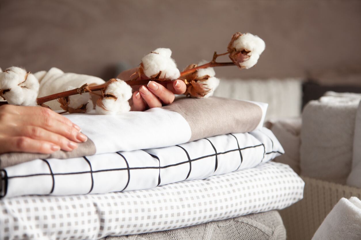 Woman holding a cotton branch with pile of neatly folded bed sheets, blankets and towels.