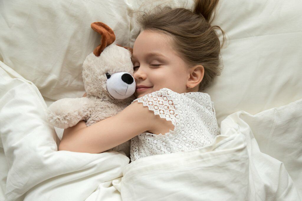 Little girl snuggles teddy bear in bed