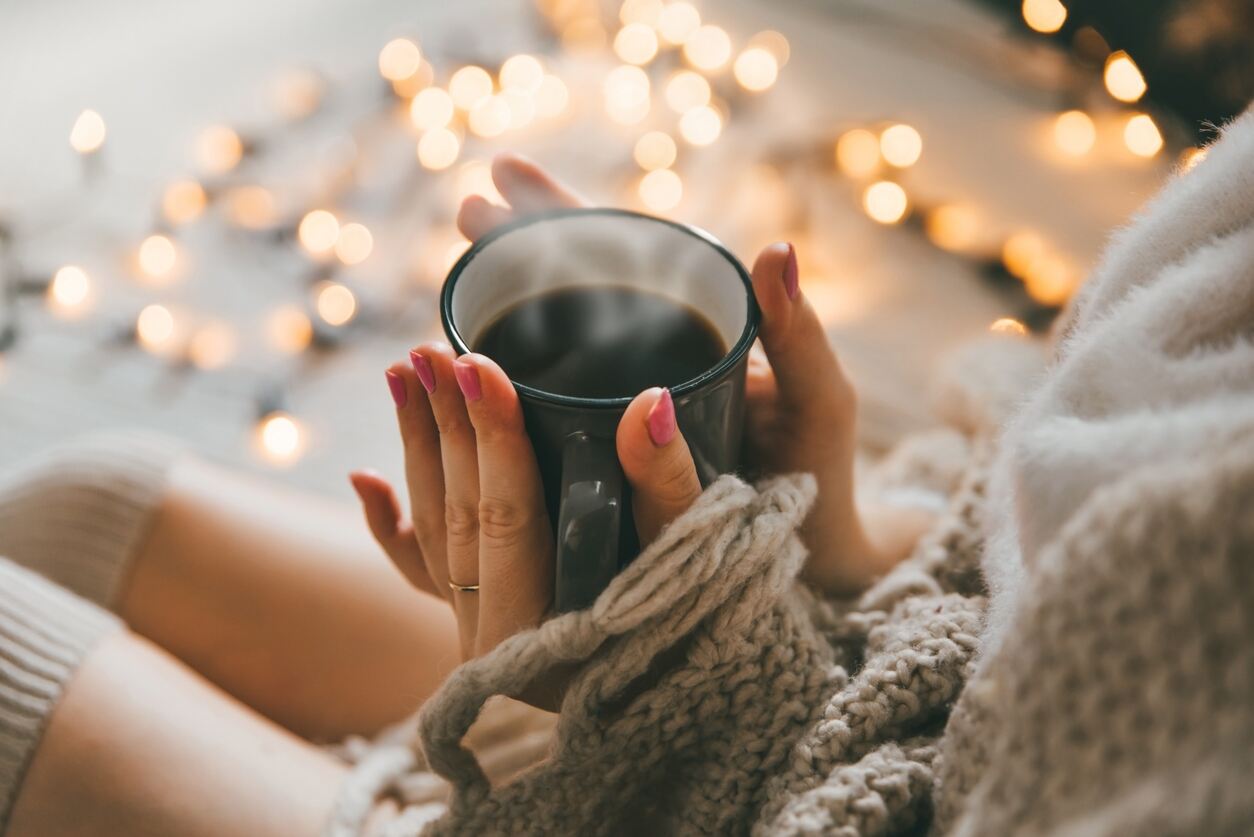 Woman holding warm drink in bedroom surrounded by fairy lights