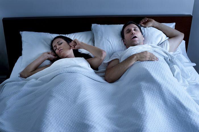 Woman puts fingers in ears as a man snores in bed