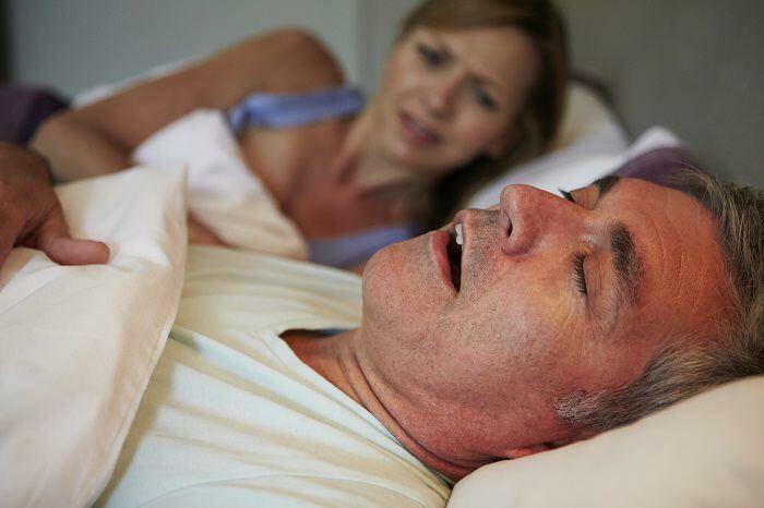Man snoring in bed as woman looks disgusted