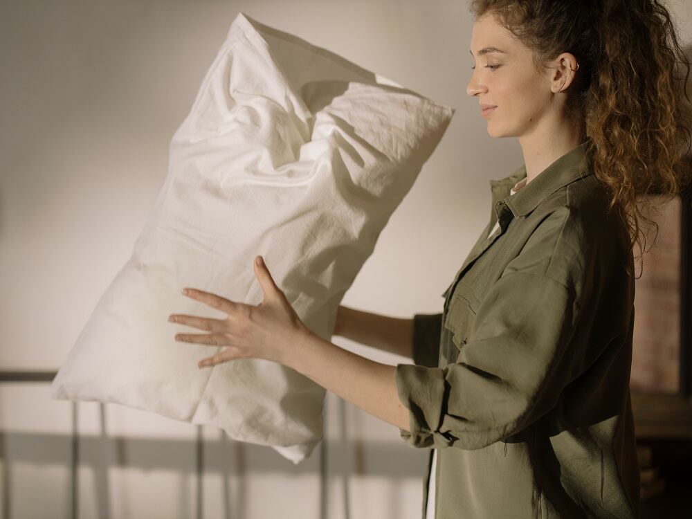 Image of woman fluffing up a pillow for a bed.